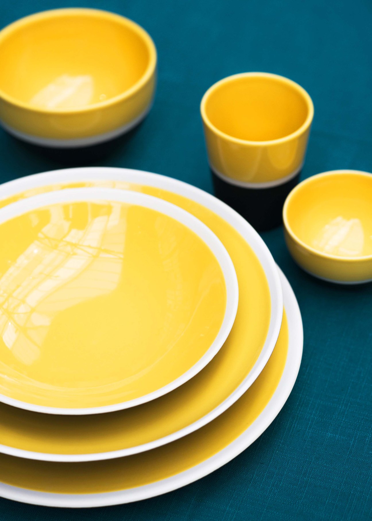 Sicilia ceramic dinnerware set in yellow and terracotta tones arranged on teal surface.