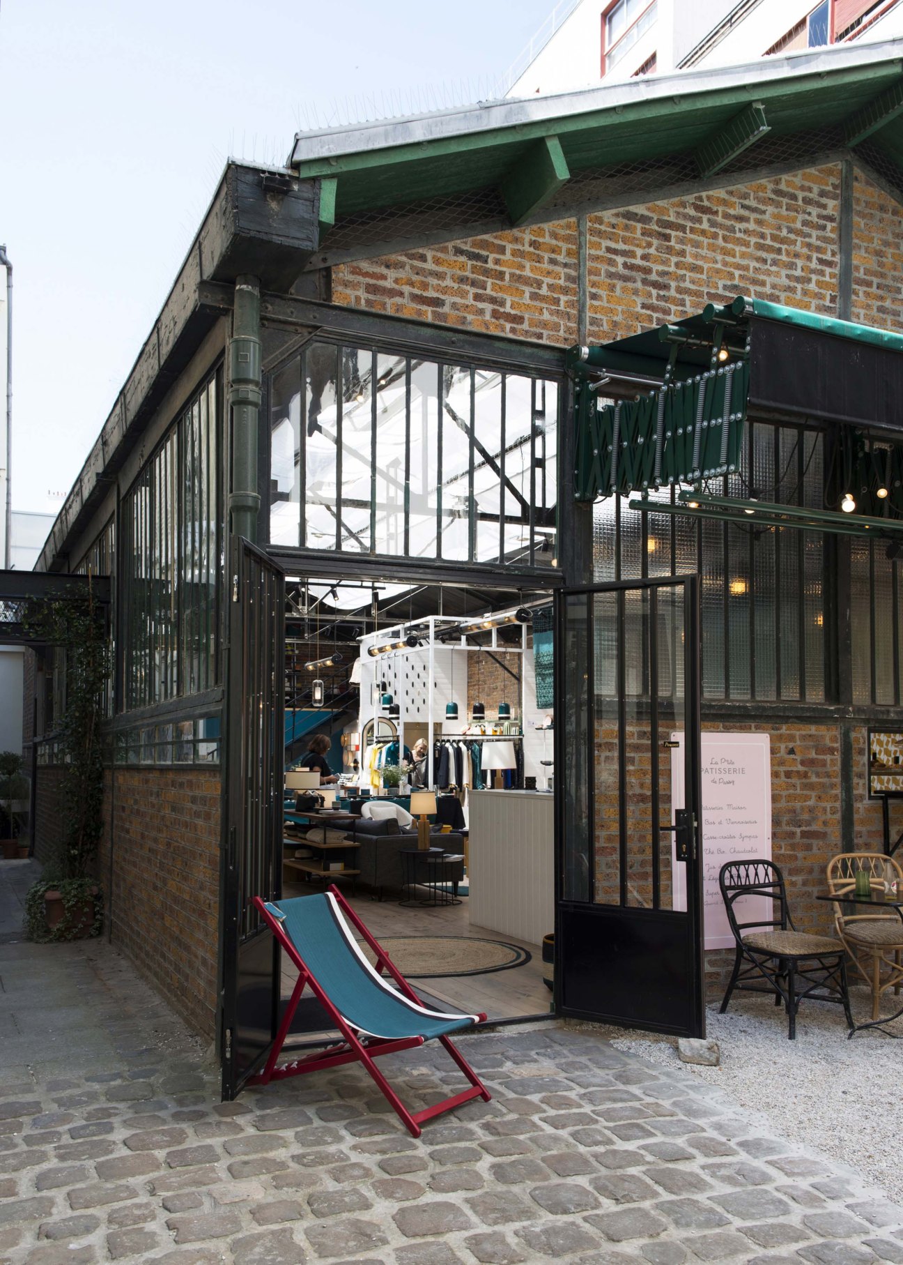 Cobblestone courtyard with green metal doors and seating area at Maison Sarah Lavoine Paris shop