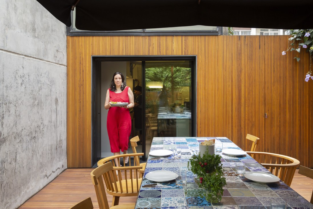 Woman in red dress standing at doorway of wooden patio with dining table set for meal