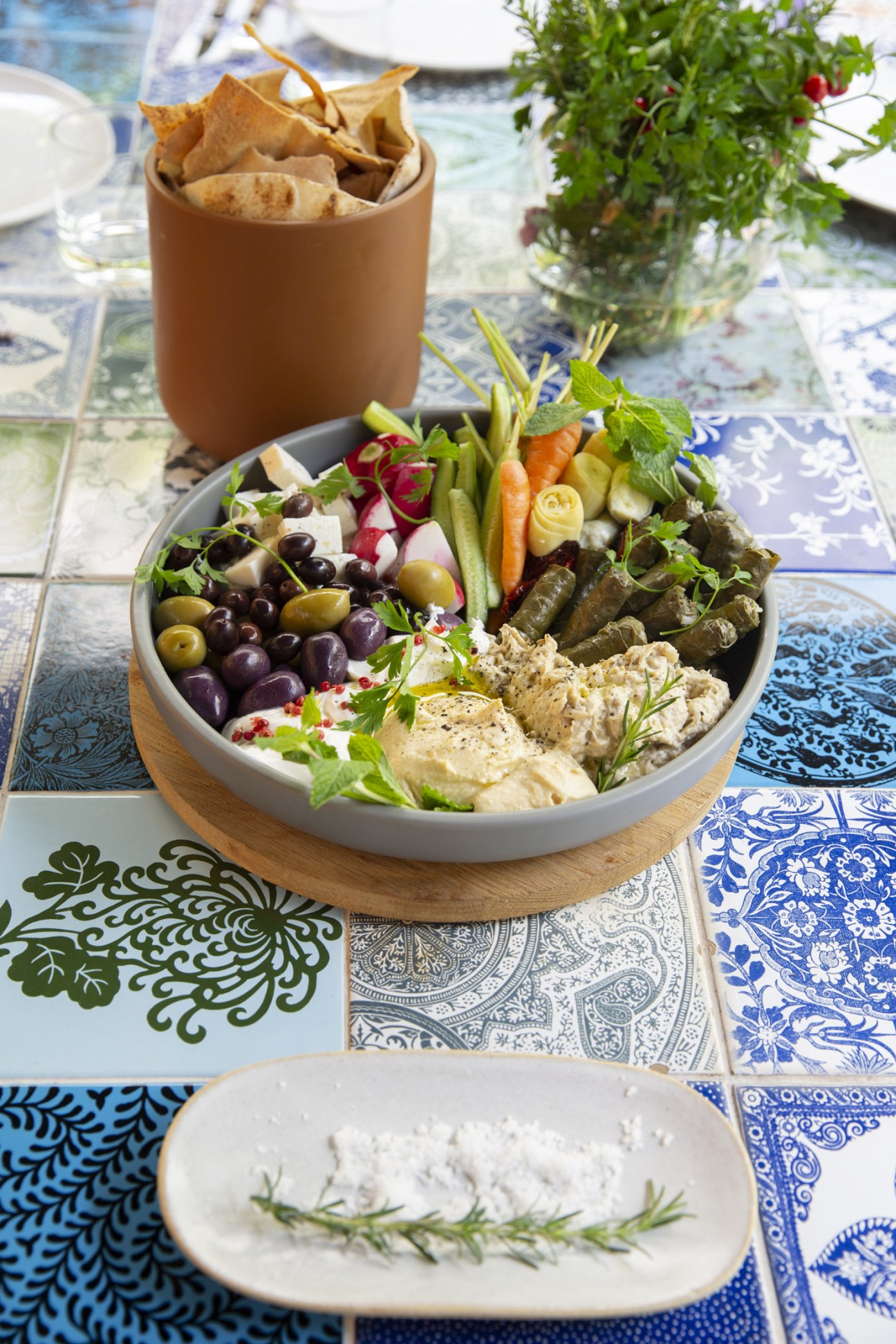 Mediterranean platter with olives, fresh vegetables, hummus and herbs on decorative blue and white tiles