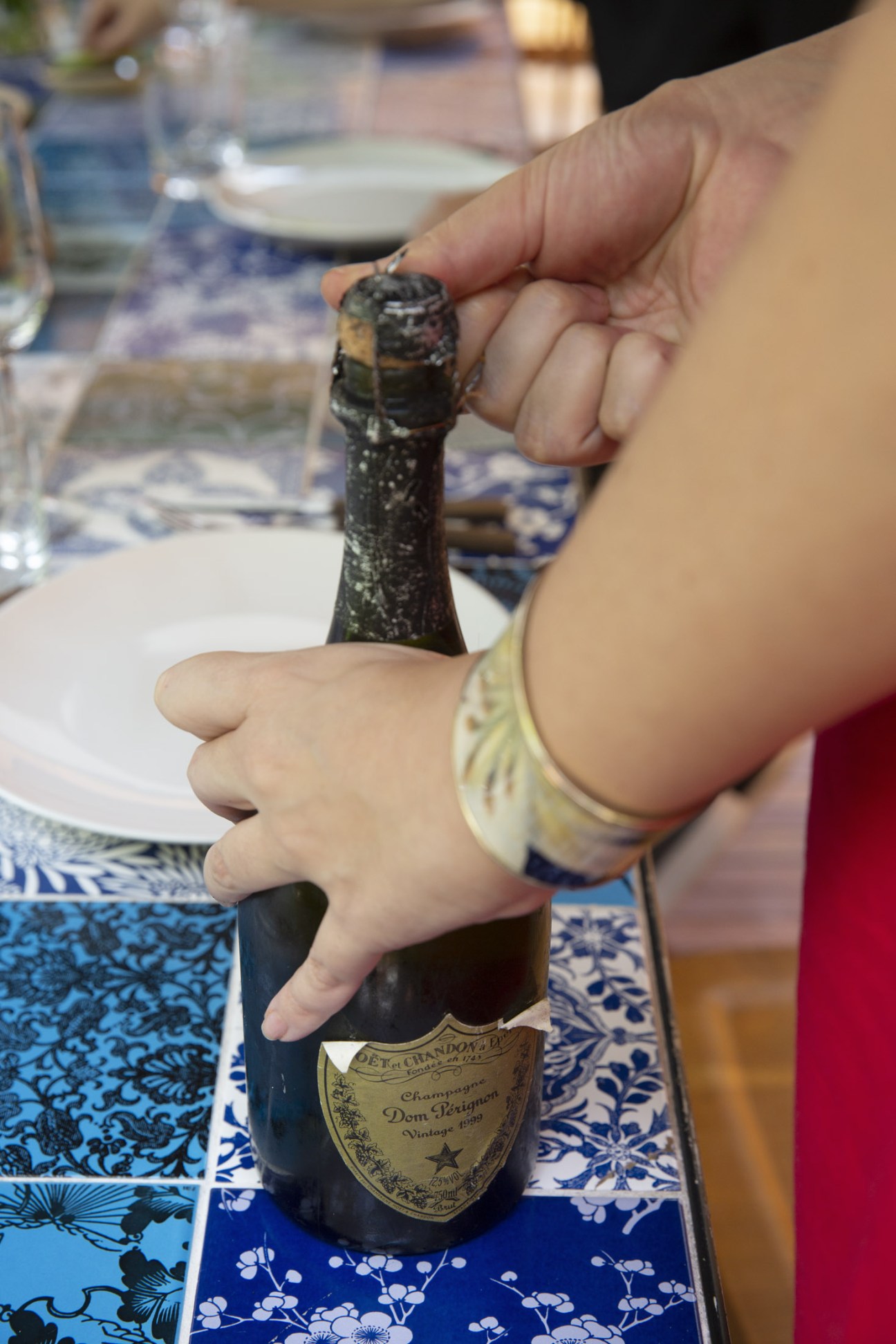 A hand holding a Dom Pérignon champagne bottle at a dining table with blue patterned placemats.