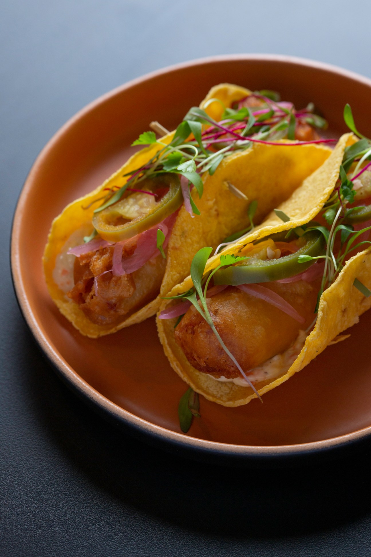 Tacos garnished with microgreens, pickled onions and jalapeños served on a brown ceramic plate