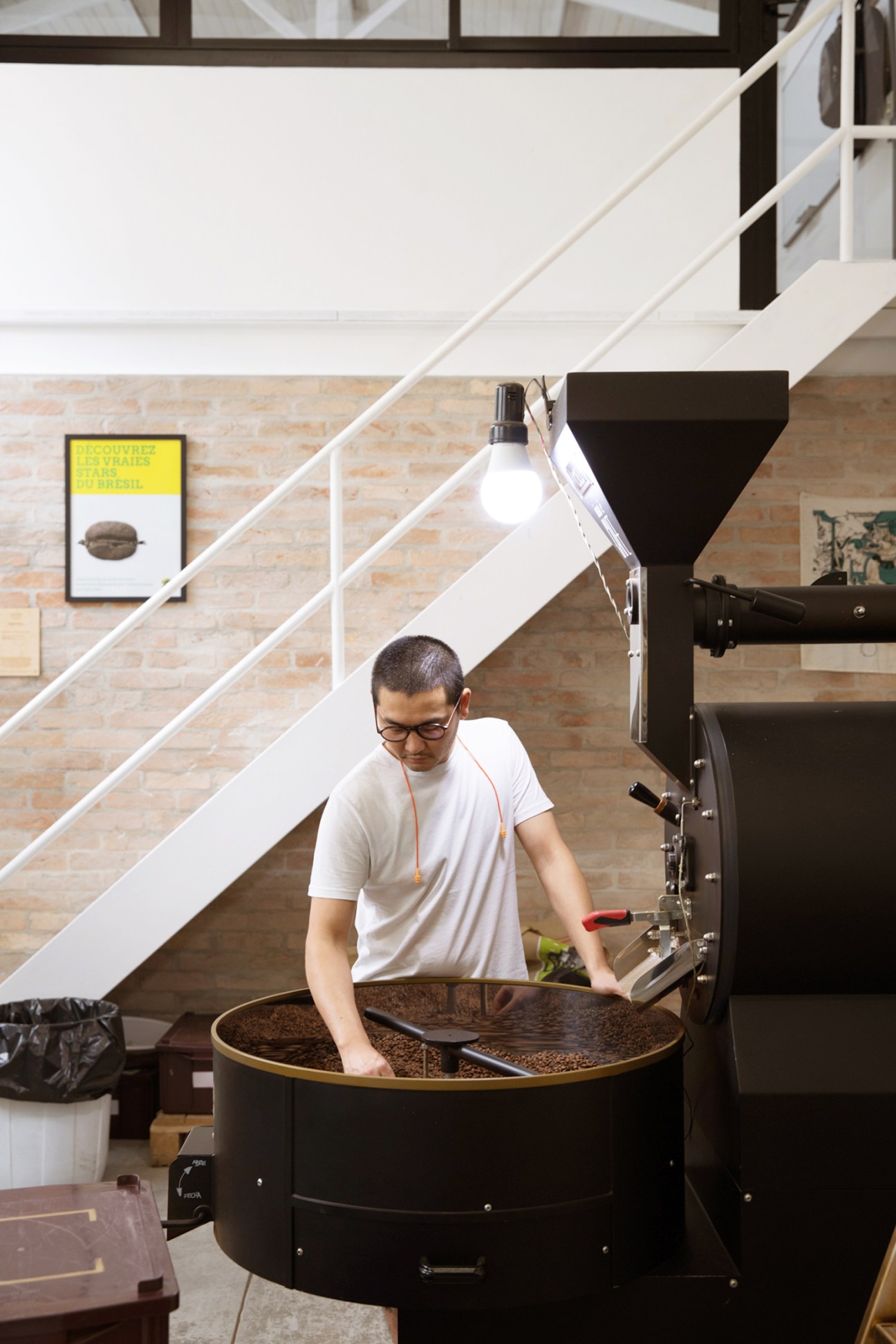 Man with glasses operating coffee roasting equipment, stirring beans in large circular roaster at Isso é Café