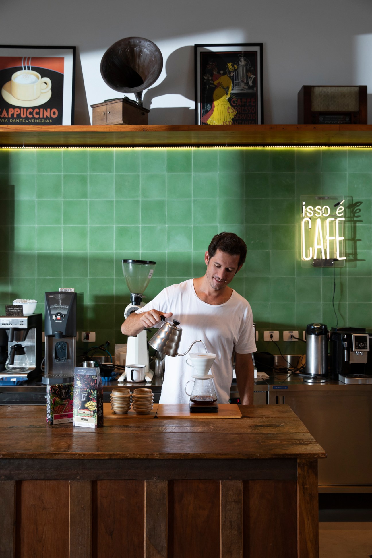 Barista pouring coffee from kettle at Isso é Café with green tiled wall and neon sign