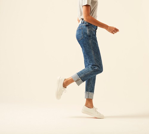 Woman wearing rolled-hem cropped jeans by Closed with white sneakers and cream shirt.
