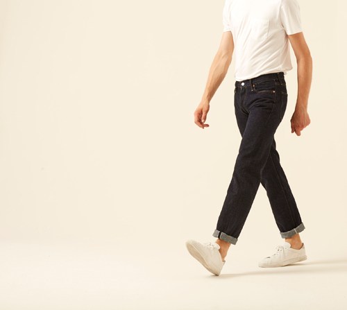 Man wearing 66 jeans by Denime in dark indigo with rolled cuffs and white sneakers
