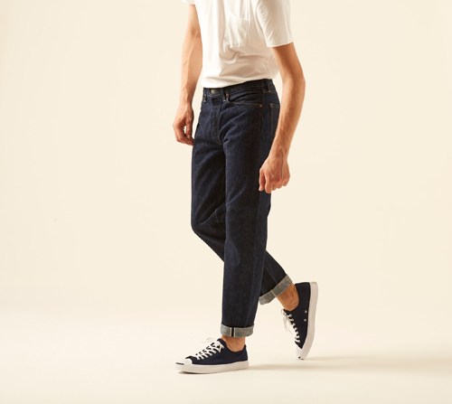 Model wearing Slim fit 107 jeans by OrSlow in dark indigo with cuffed hem and black sneakers.