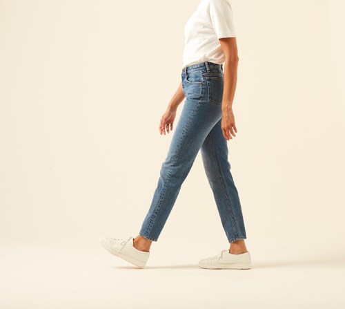 Person wearing AMI fit jeans in dark wash with white t-shirt and sneakers against cream background
