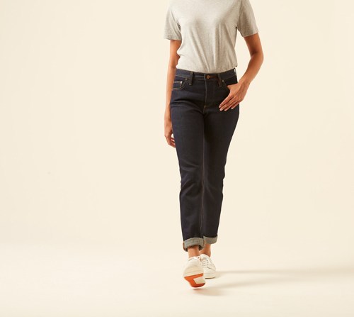 Woman wearing The Coda jeans by Hiut Denim Co in dark indigo with cuffed ankles and white sneakers.