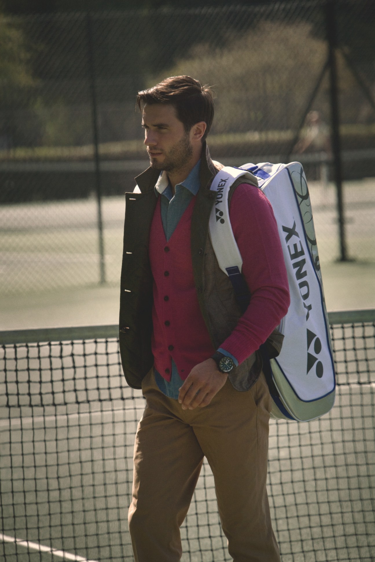 Male model at tennis court wearing Sophnet vest, The Inoue Brothers cardigan, Folk shirt, Ralph Lauren trousers and Yonex racquet bag.