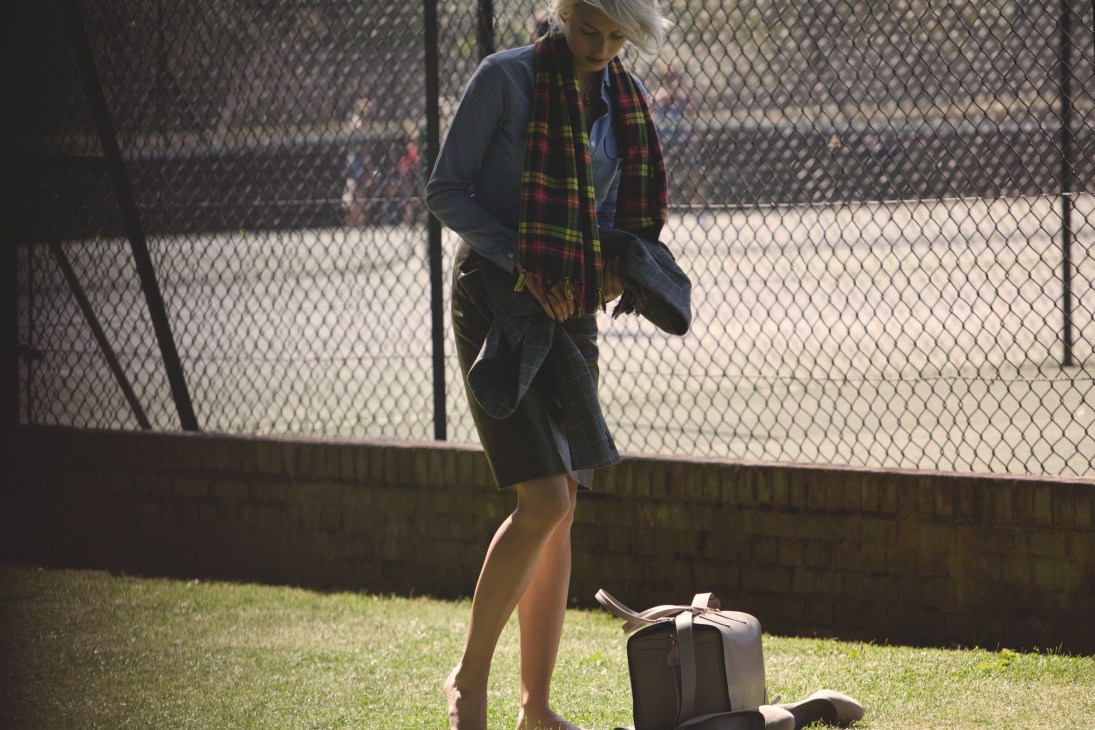 Woman in Oscar de la Renta skirt and Designer accessories at tennis court with bag.