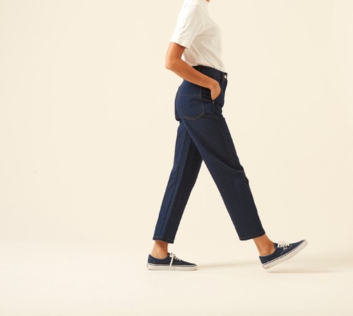 Person wearing Lemaire twisted pants in dark navy with white t-shirt and navy sneakers, side profile walking stance.