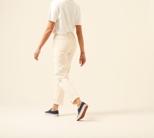 Person wearing white shirt and cream straight-leg jeans by Arket with rolled ankles and navy sneakers.