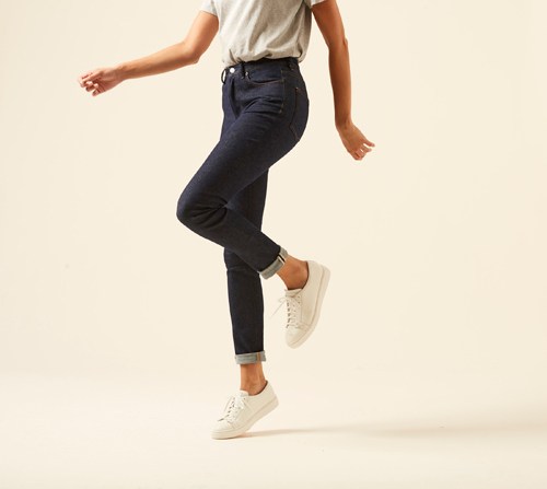 Woman wearing dark Peg jeans by Acne Studios in high-waisted tapered fit with white sneakers.