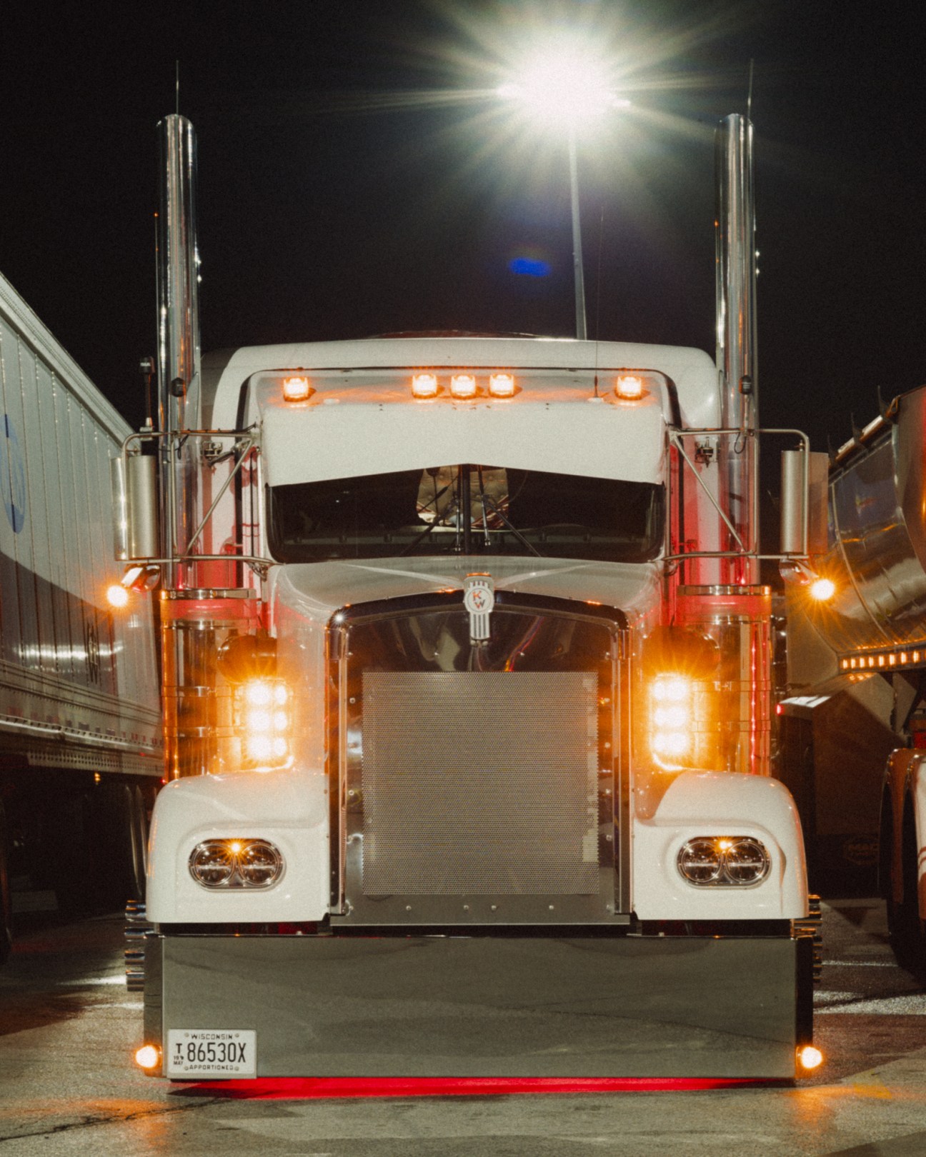 Front view of a customised white and red Kenworth truck parked at night under bright floodlights.