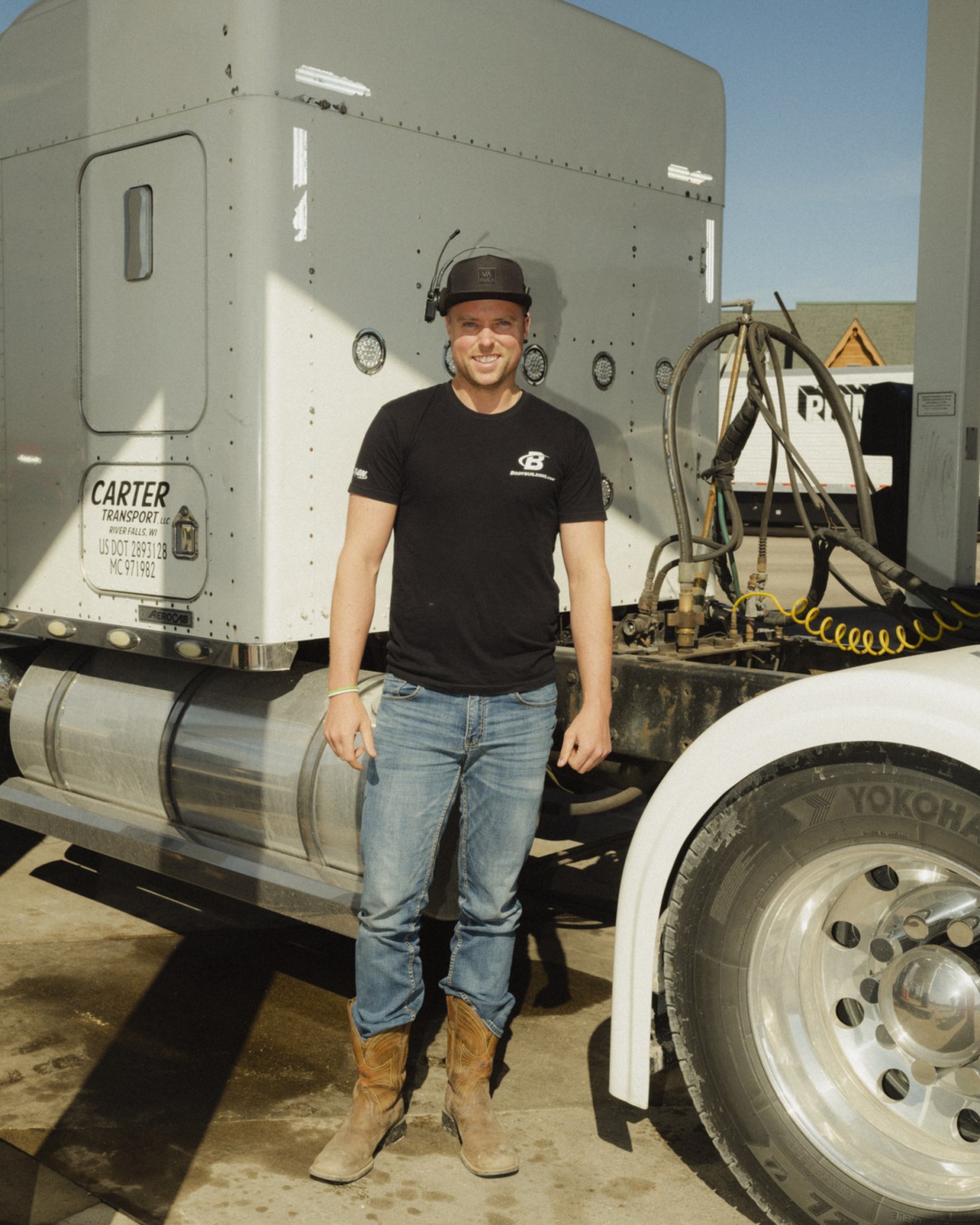 A truck driver standing in front of his white Carter Transport semi-truck cab on a sunny day.