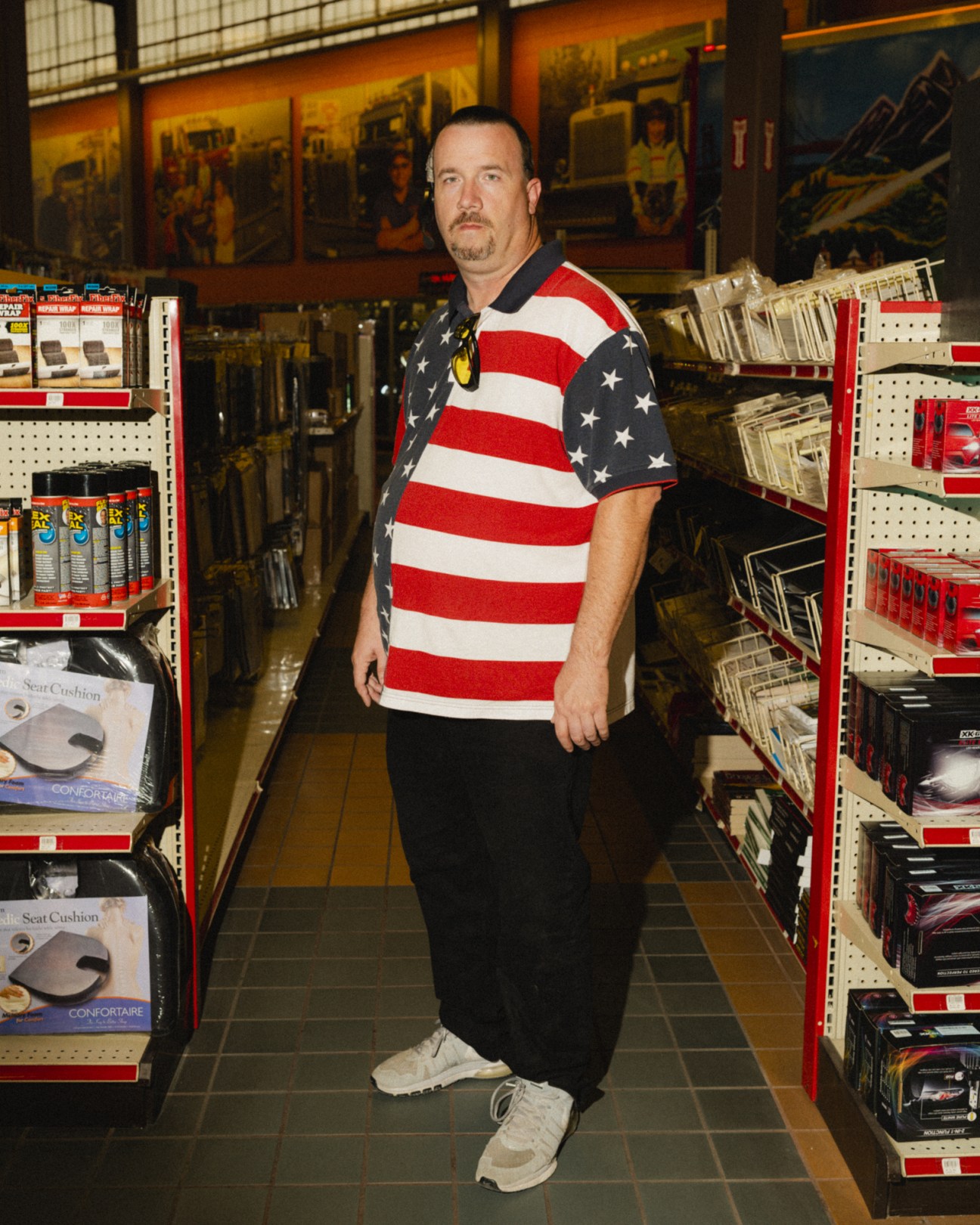 Man wearing American flag shirt standing in truck parts showroom with shelves of merchandise.