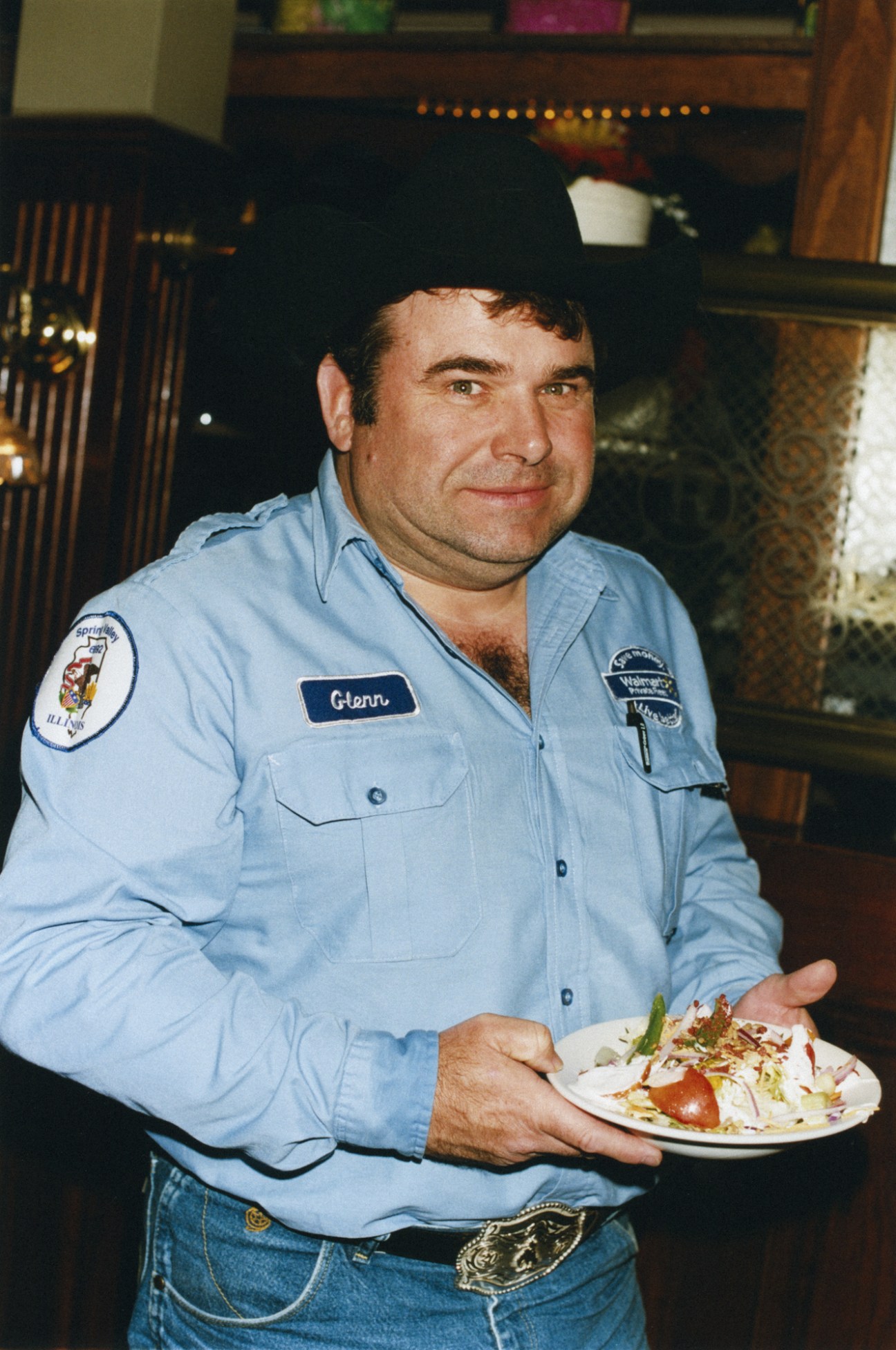 Man in light blue work shirt holding a plate of salad at a restaurant counter