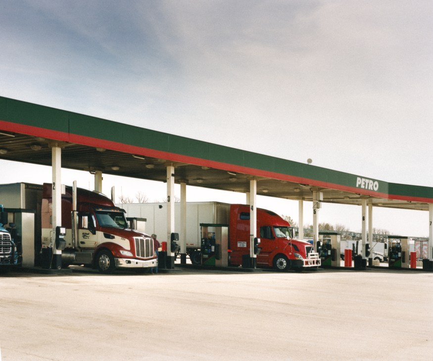 Semi-trucks fueling at a covered fuel island with green and red canopy at Trail's Travel Center.