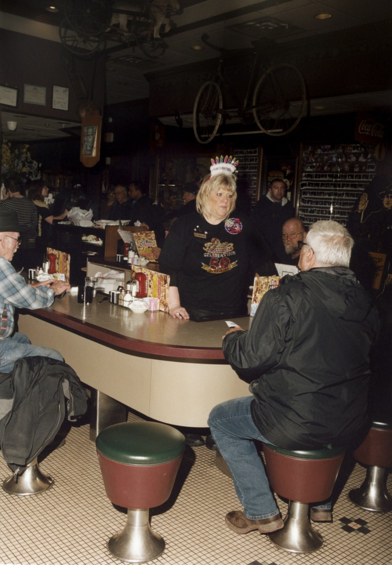Loud Mary, a waitress wearing a birthday crown, serves customers at the counter of R Place restaurant.