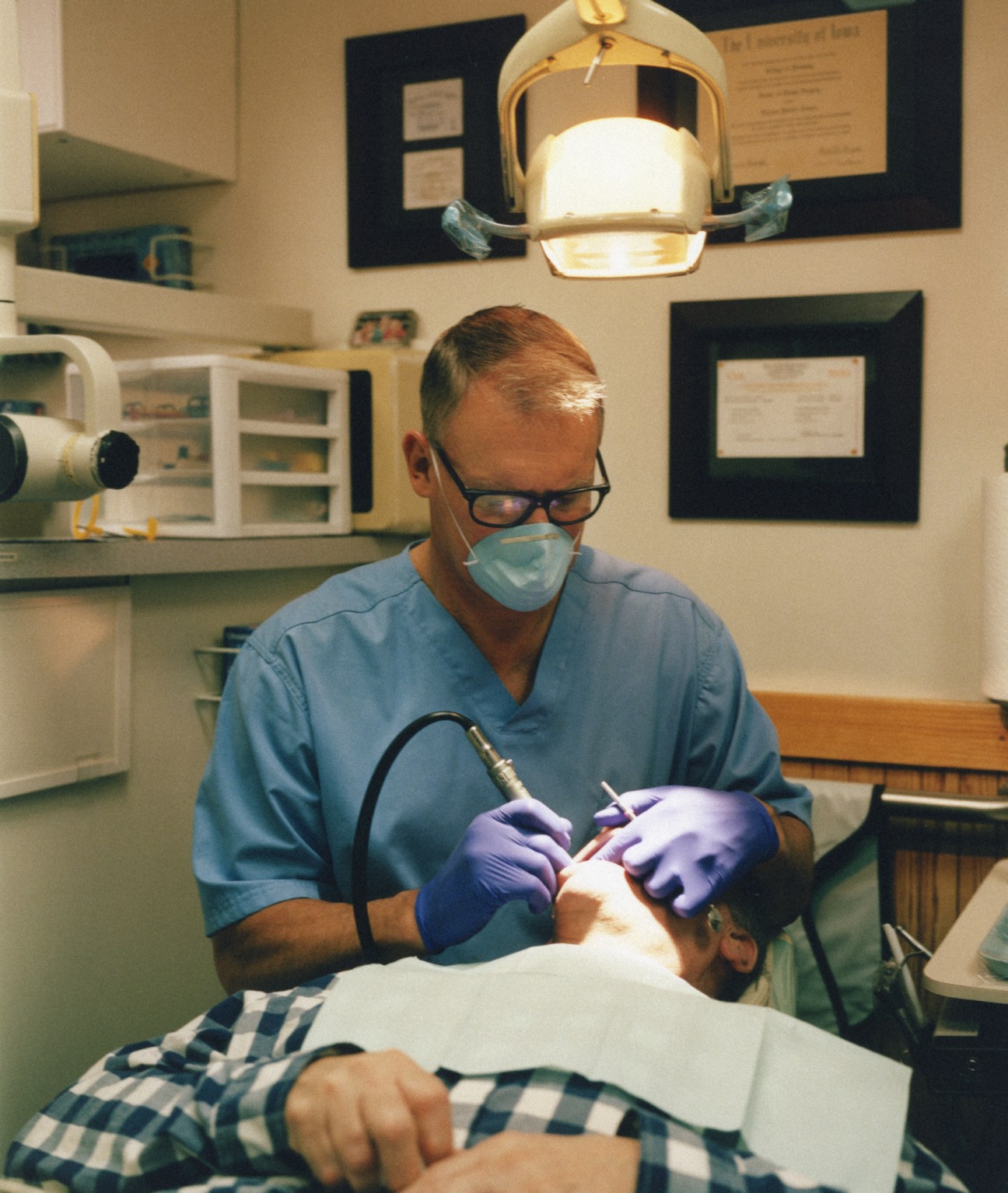 Dentist Thomas Roemer wearing blue scrubs, mask and gloves treats a patient in his dental office at Iowa 80 truckstop.