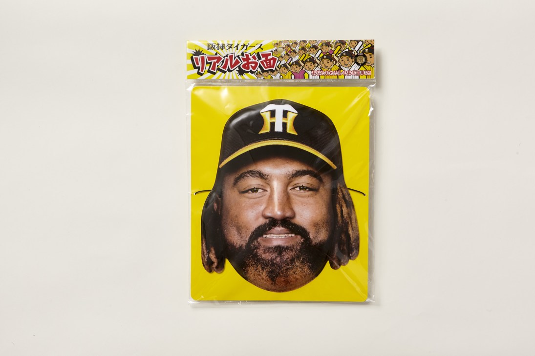 Plastic face mask of Hanshin Tigers pitcher with long dark hair and beard wearing team cap.