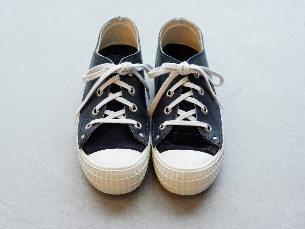 Navy canvas sneakers with white laces and cream rubber soles on gray background