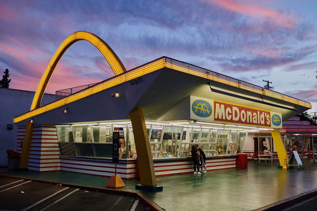 Googie-style McDonald's building in Downey with distinctive yellow neon arch, red and white striped walls, and space-age design at dusk.
