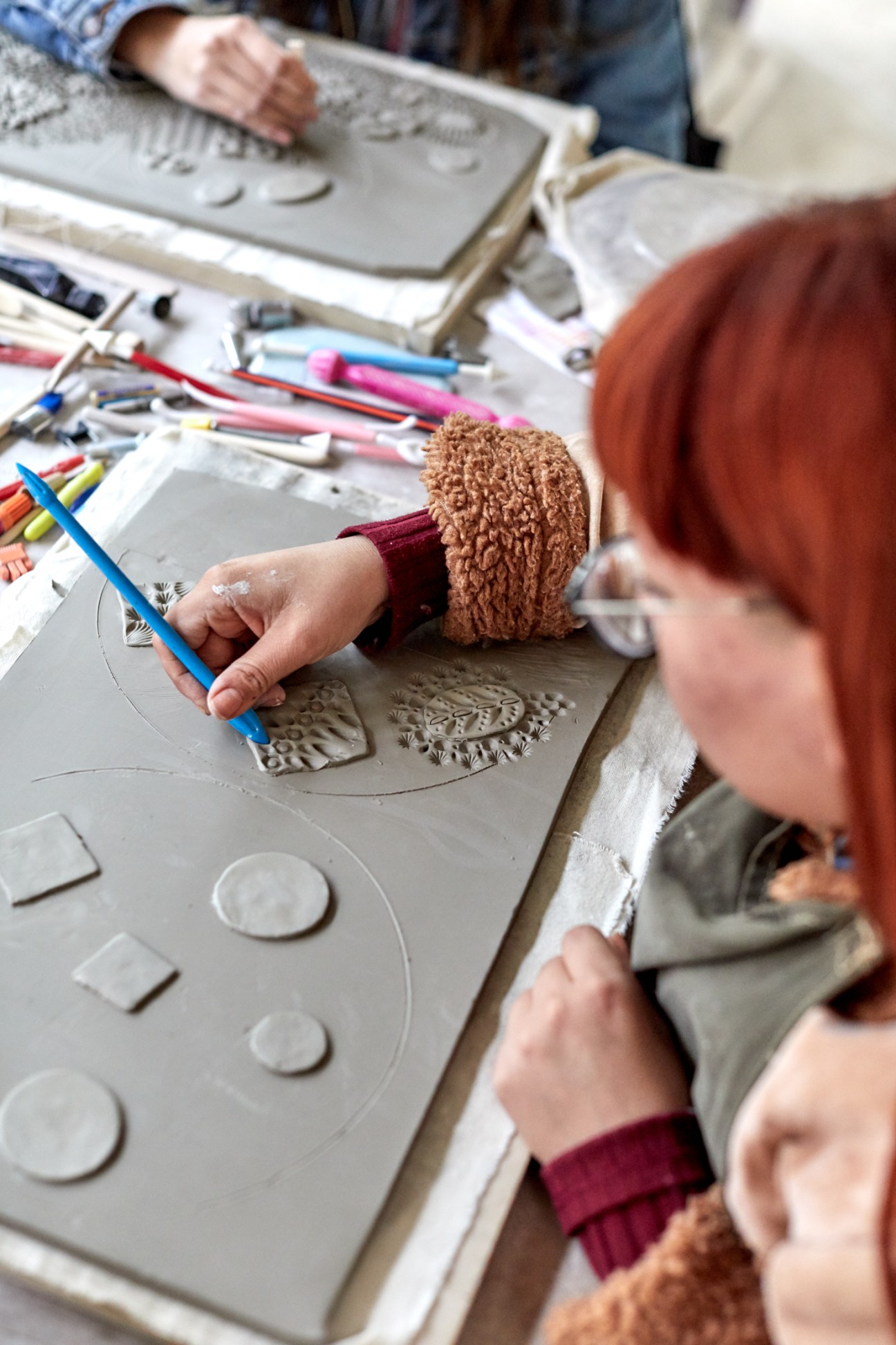 Person working with clay tools to create decorative patterns on ceramic pieces at pottery studio workspace