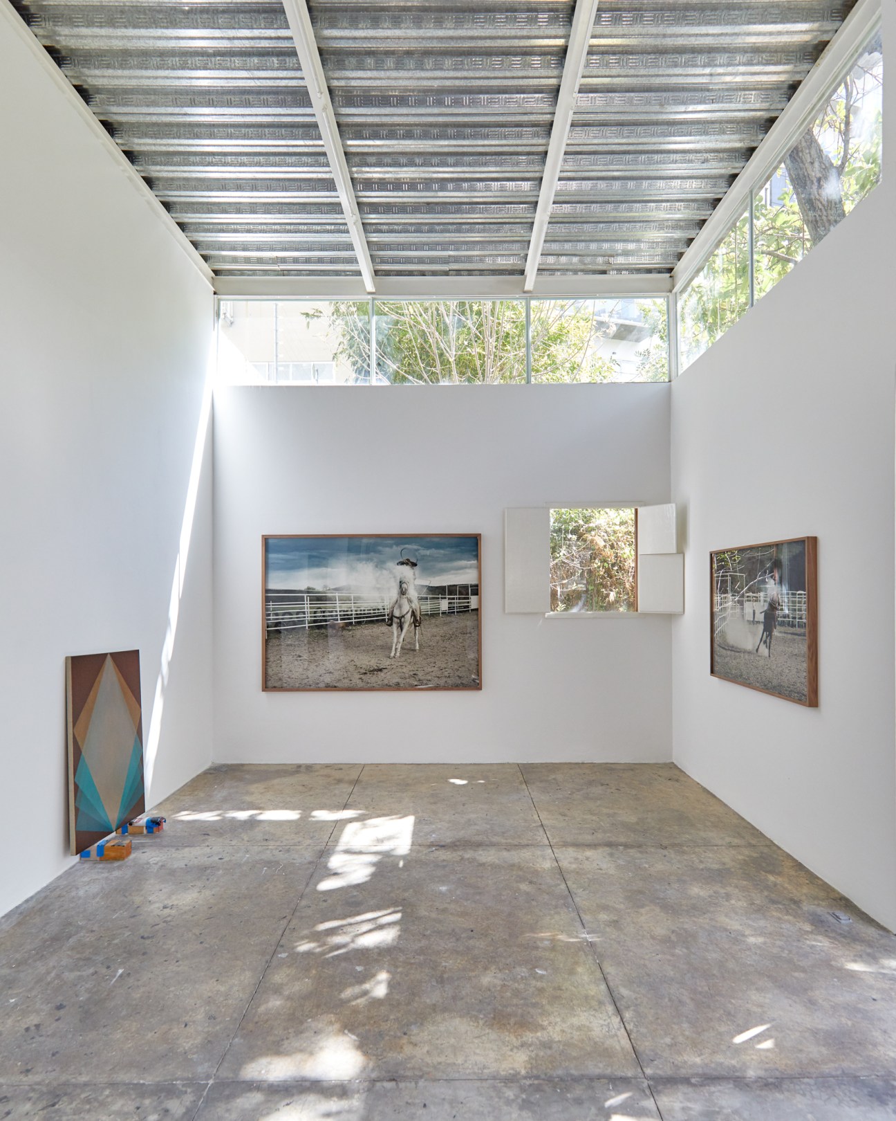 Modern gallery space with concrete floor, white walls displaying horse photographs, and partially open ceiling