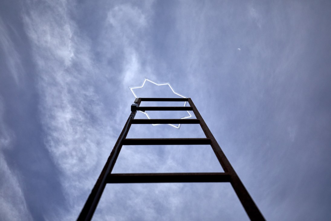 A black ladder extends upward against a cloudy blue sky with a translucent star-shaped outline at the top
