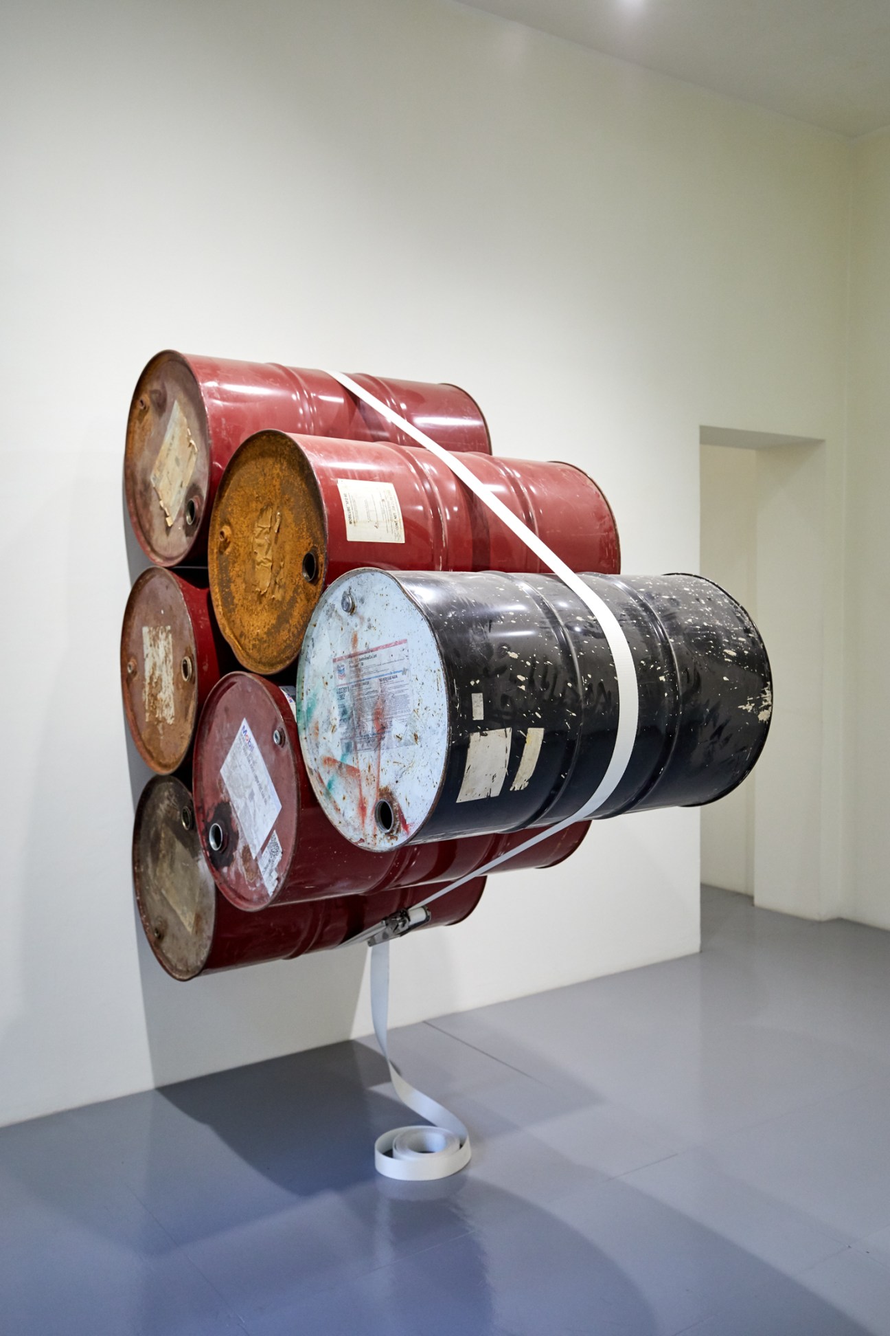 Industrial oil drums bundled with white strapping displayed as contemporary art installation in white gallery space