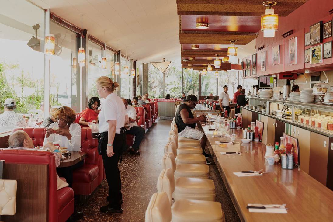 Interior of Pann's diner showing red vinyl booths, counter seating, pendant lighting, and diners in mid-century modern setting