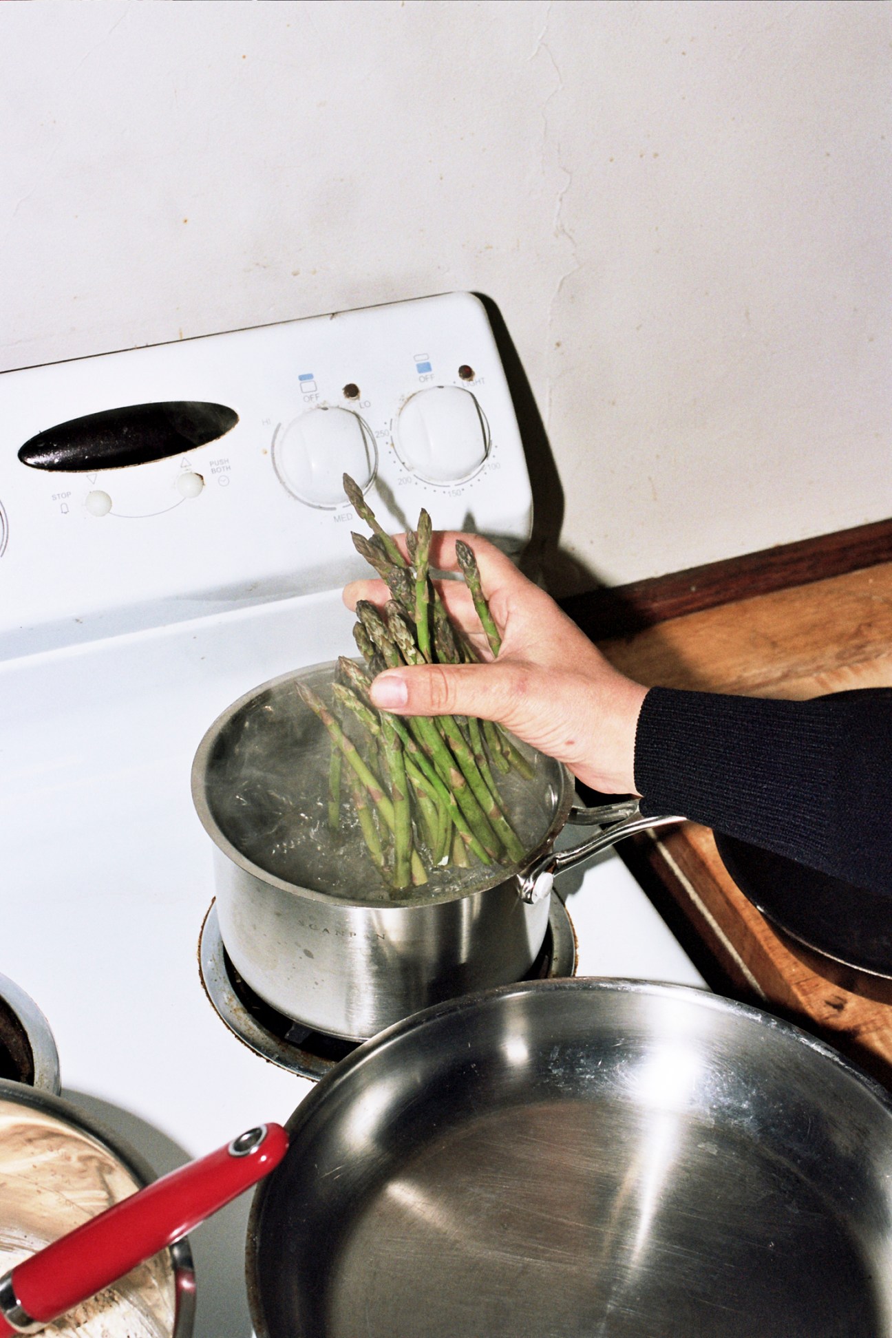 Hand placing fresh asparagus spears into a pot of boiling water on a stovetop