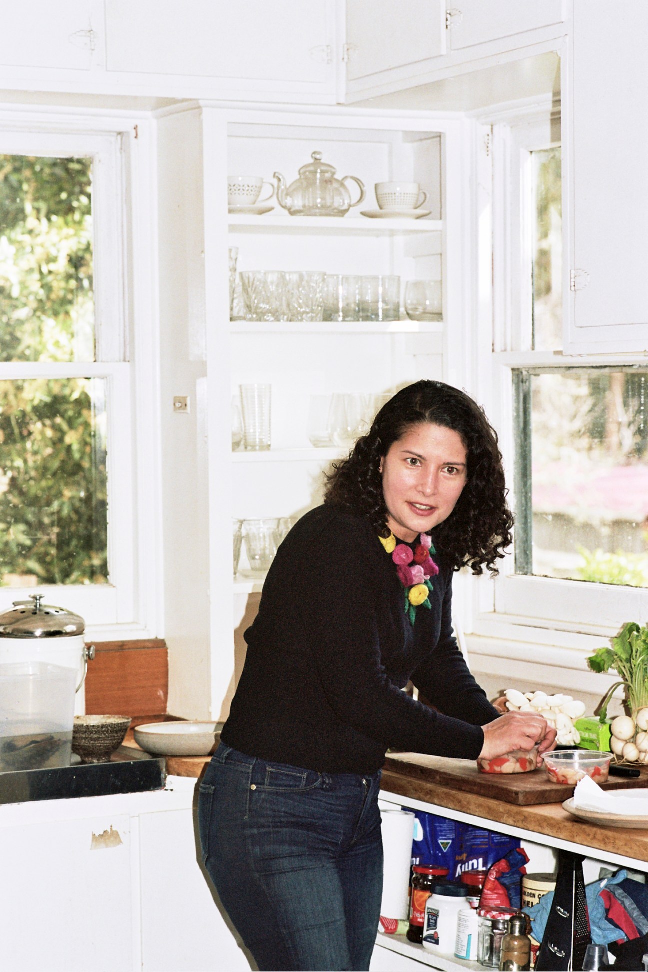 Chef Analiese Gregory preparing food in her bright white kitchen with glass-front cabinets and wooden countertops