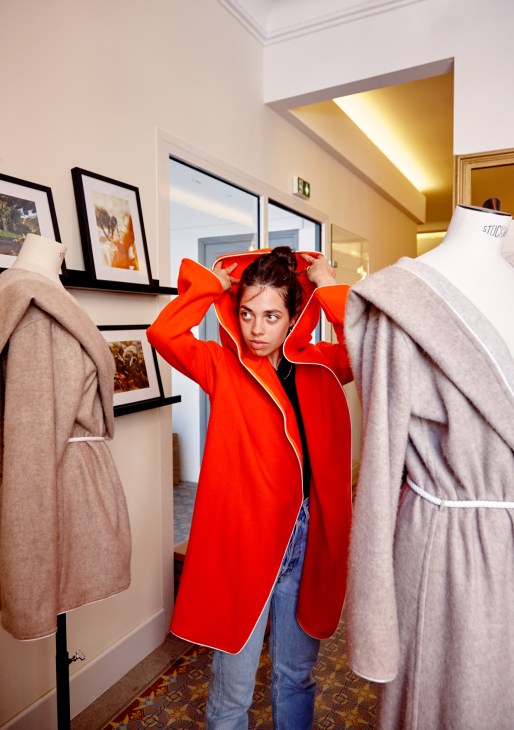 A woman trying on a bright red wool coat in a modern boutique with displayed jackets.