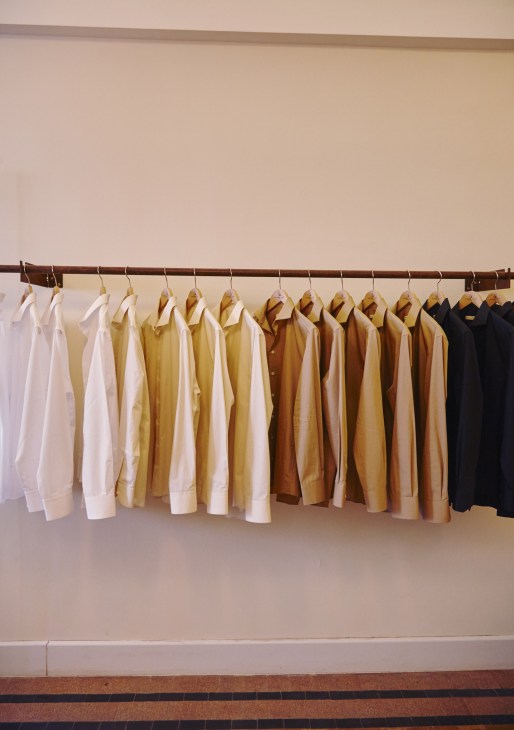 Cotton shirts in neutral tones displayed on wooden hangers at Maison Rucher boutique.