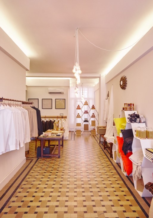 Interior of Maison Rucher shop with white clothing on left rack, geometric patterned floor, and pendant lighting.