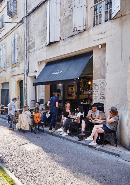 Diners seated at tables outside Bardvin restaurant on a narrow Arles street.
