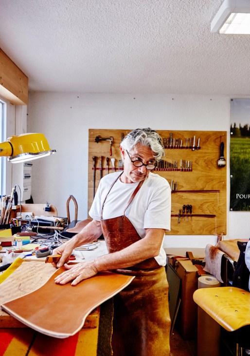 Christophe Berti working with leather at his workbench in a bright atelier with tool pegboards.