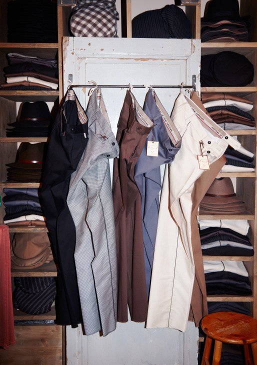 Horsemen's trousers hanging on a rail in Le Gardian's shop, with shelves of folded garments behind.