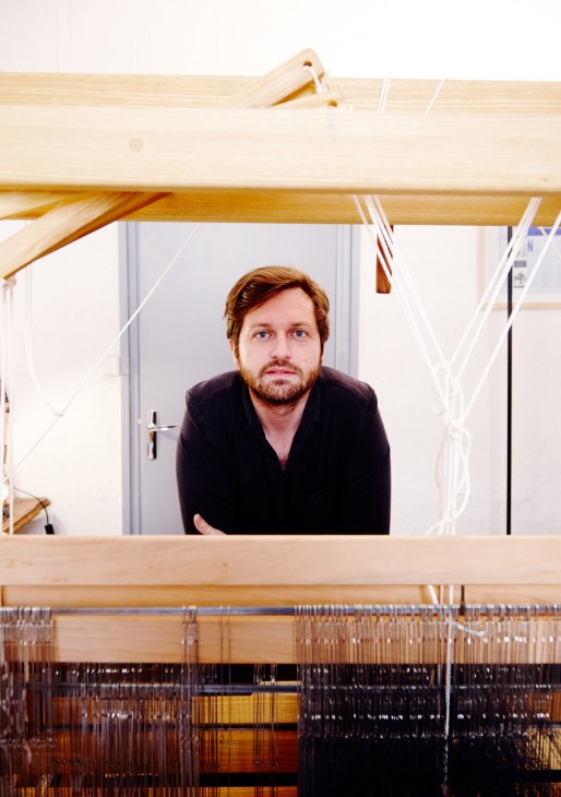 Guillaume Sagot, founder of Ateliers Denim, standing behind a wooden weaving loom with threads.