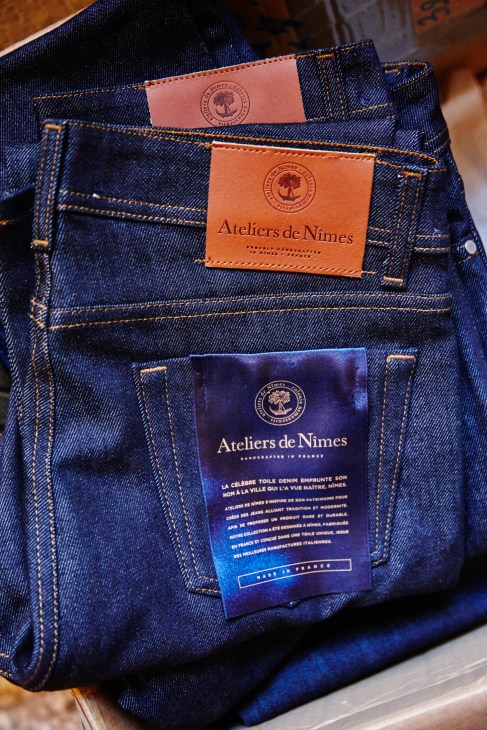 Close-up of Ateliers de Nîmes denim jeans with leather and fabric labels in various colors.