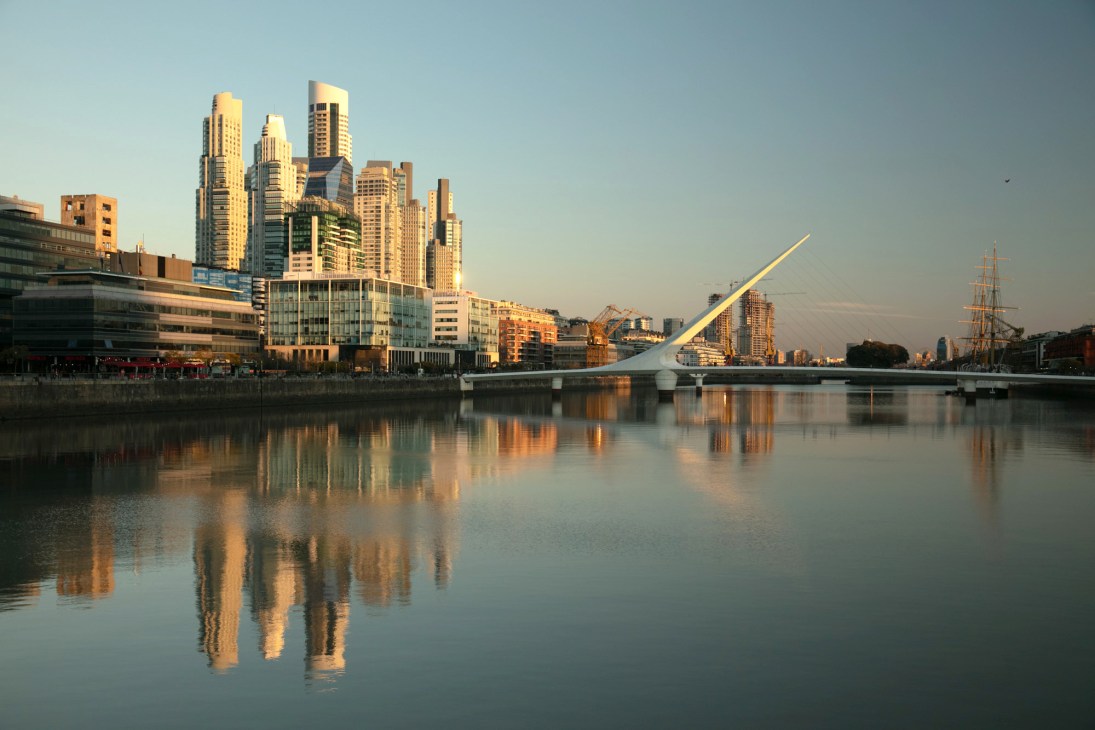 Buenos Aires skyline at sunrise with modern high-rise buildings reflected in still water and a modern bridge spanning across.