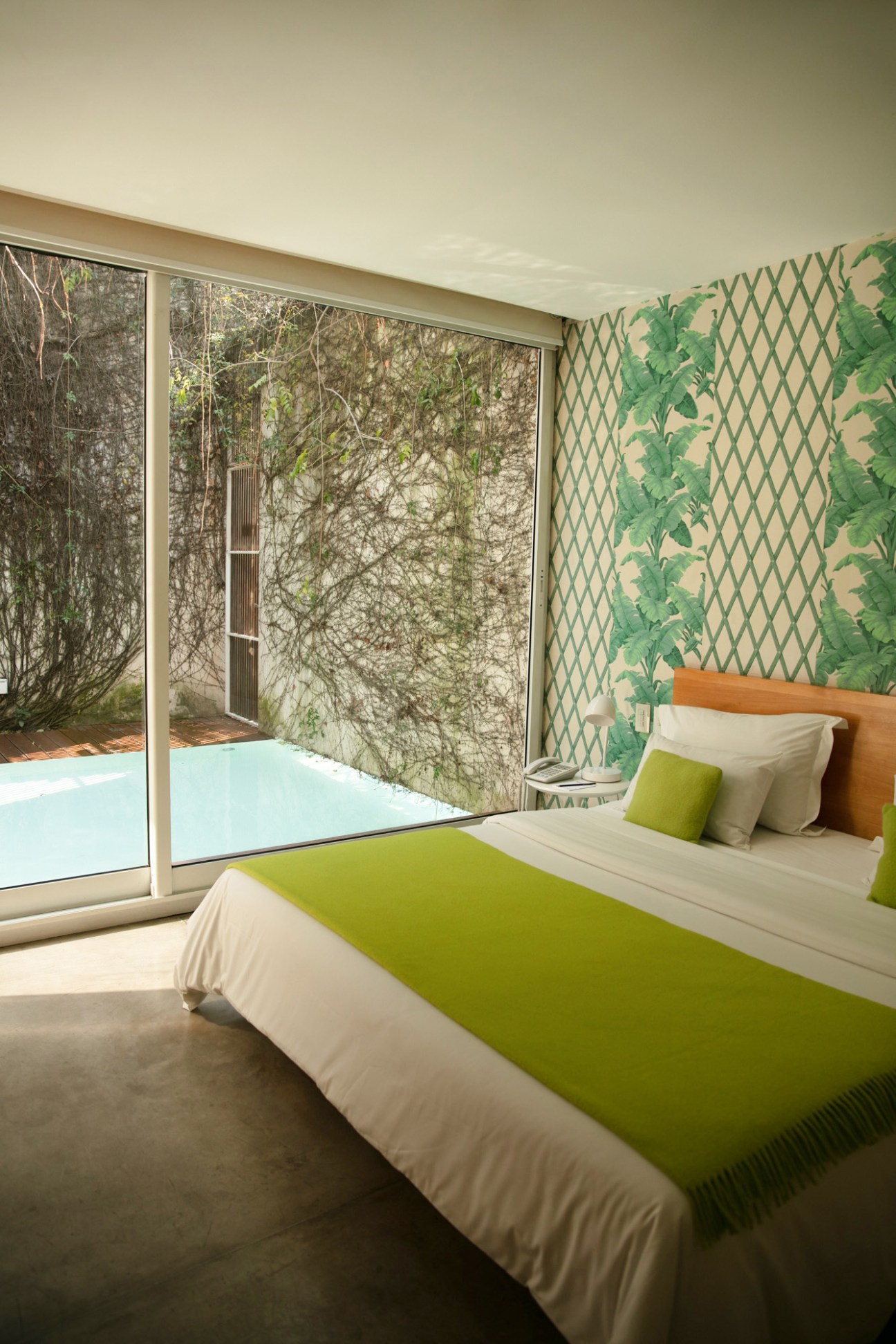 Modern bedroom at Home hotel with green bedding, patterned wallpaper, and large window overlooking garden.