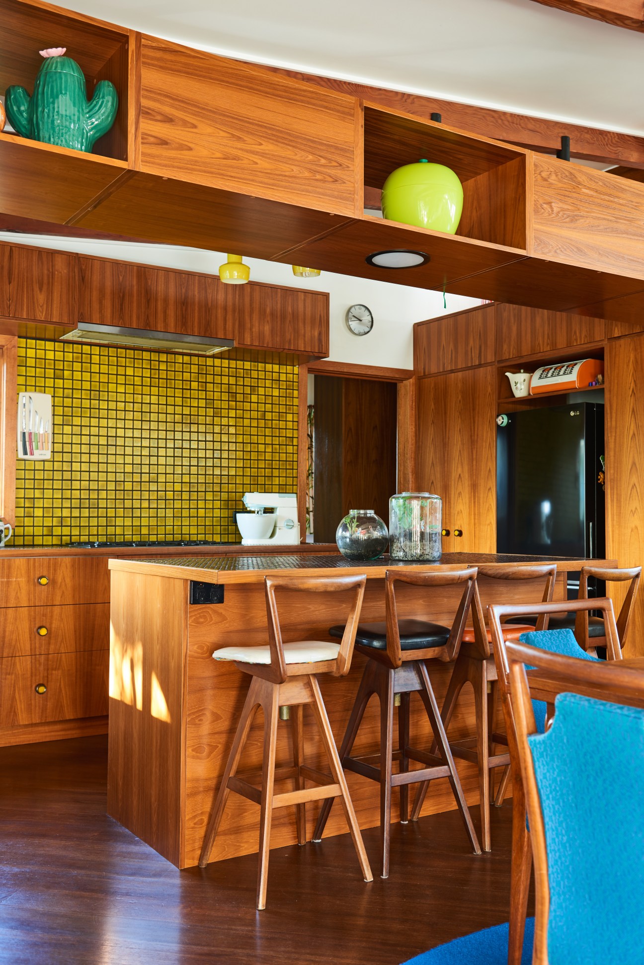 Mid-century modern kitchen with bright yellow tile backsplash, wood cabinetry, and mid-century bar stools.