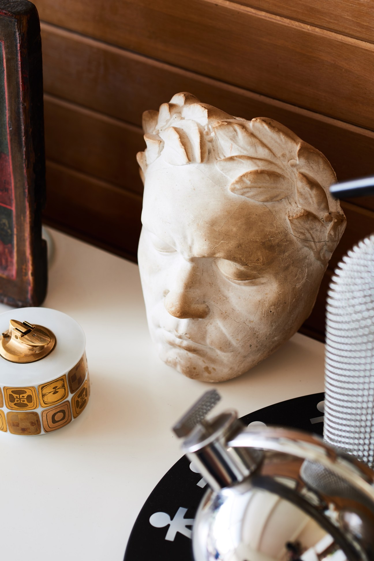 Plaster cast bust sculpture displayed among decorative objects on a shelf.