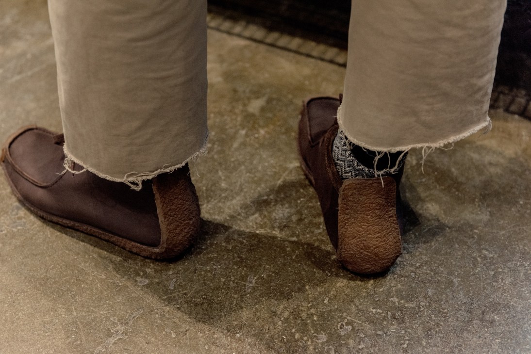 Person wearing cream-colored ripped cutoff jeans and brown leather shoes standing on pavement.