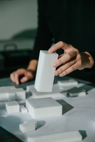 Hand placing white architectural model blocks on a table with scattered miniature building components