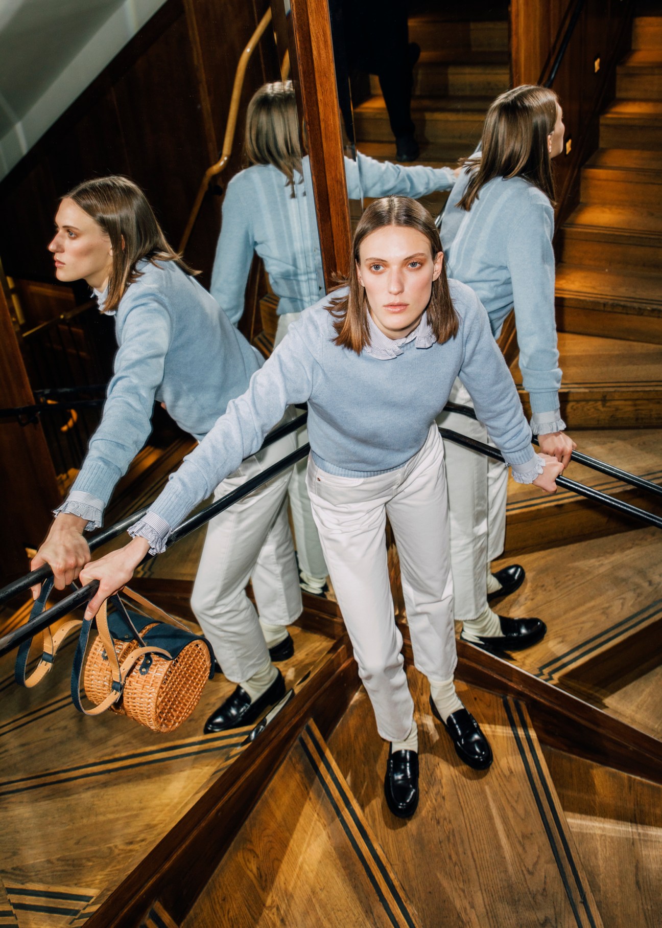 Woman in light blue sweater and beige trousers with wicker bag sitting on wooden stairs